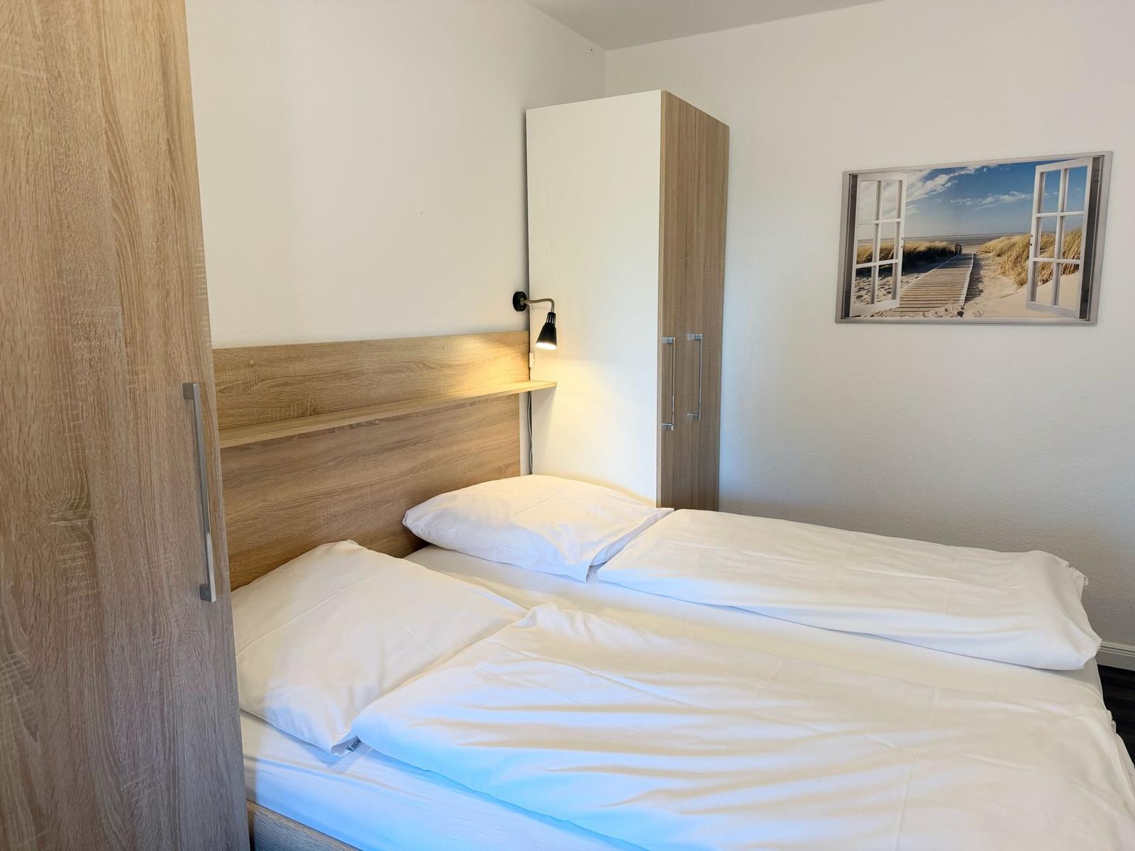 Schlafzimmer mit Doppelbett, Holzgestell und Wandbild. Neben dem Bett steht ein Schrank.