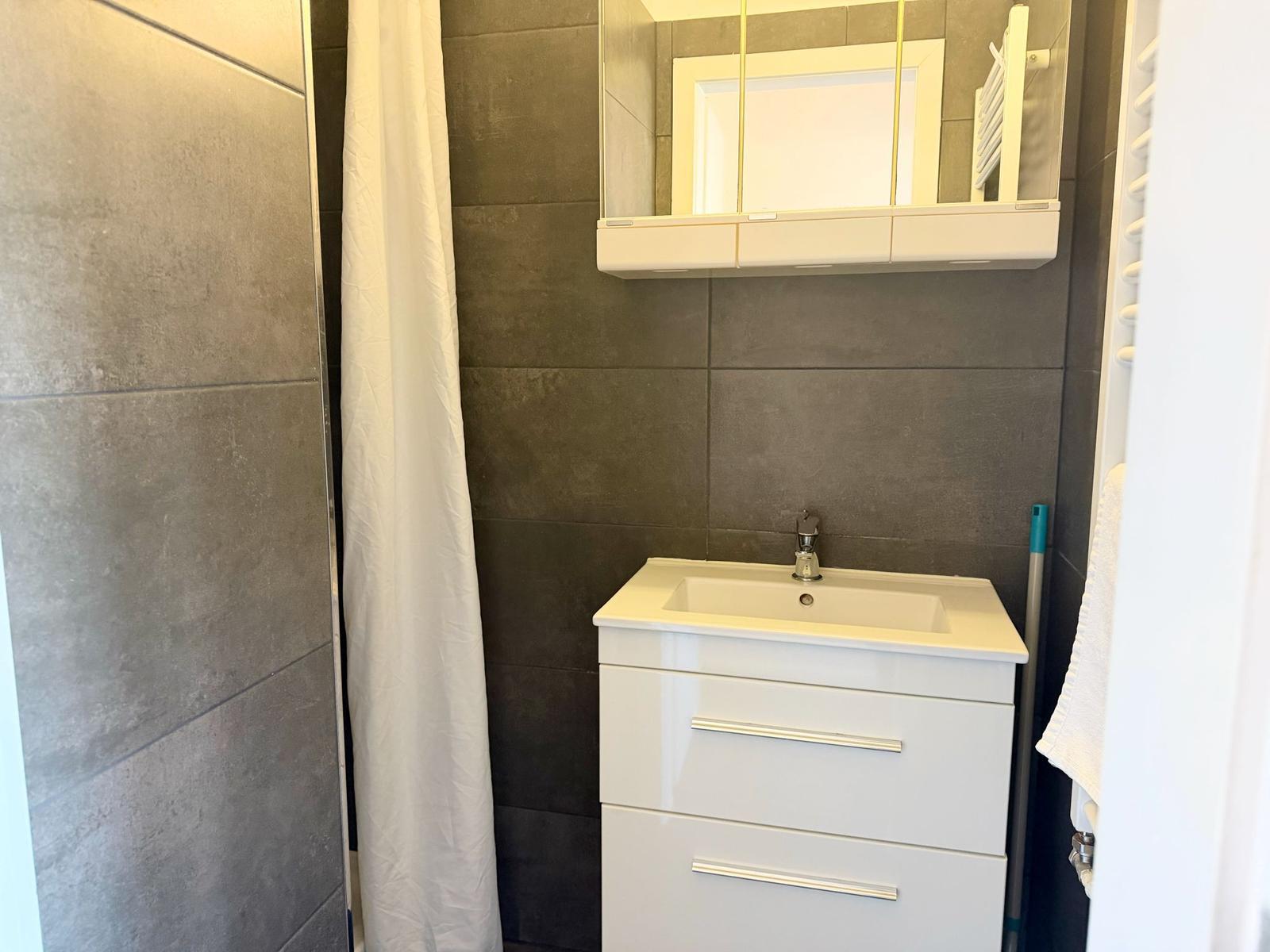 Badezimmer mit weißem Waschtisch, Spiegel und Duschvorhang.