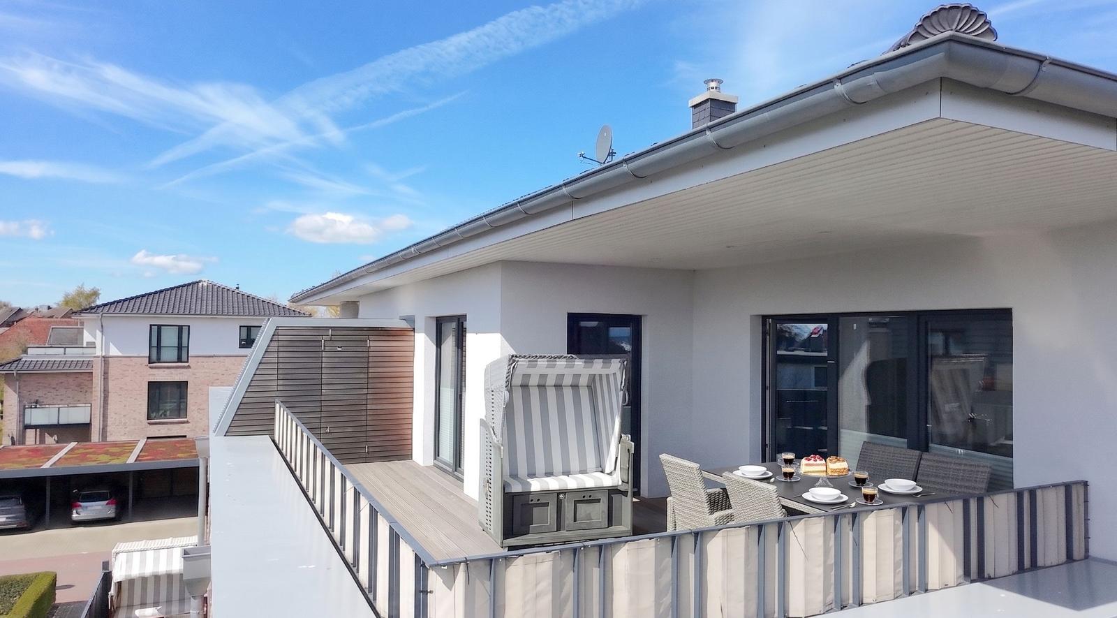 Terrasse mit Liegestuhl und Tisch für sechs Personen unter blauem Himmel.