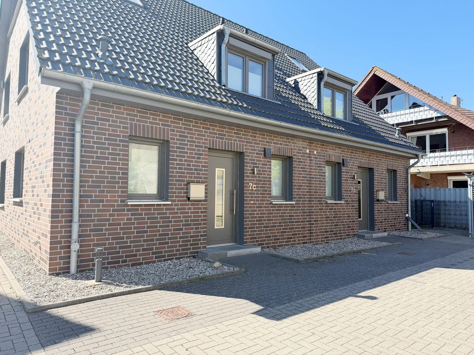 Moderne Wohnhaus mit Ziegelfassade und Dachfenstern. Zwei Eingänge mit Hausnummern.
