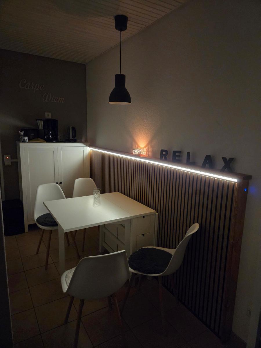 Essbereich mit Tisch, Stühlen und beleuchteter Wand mit Relax-Schriftzug.