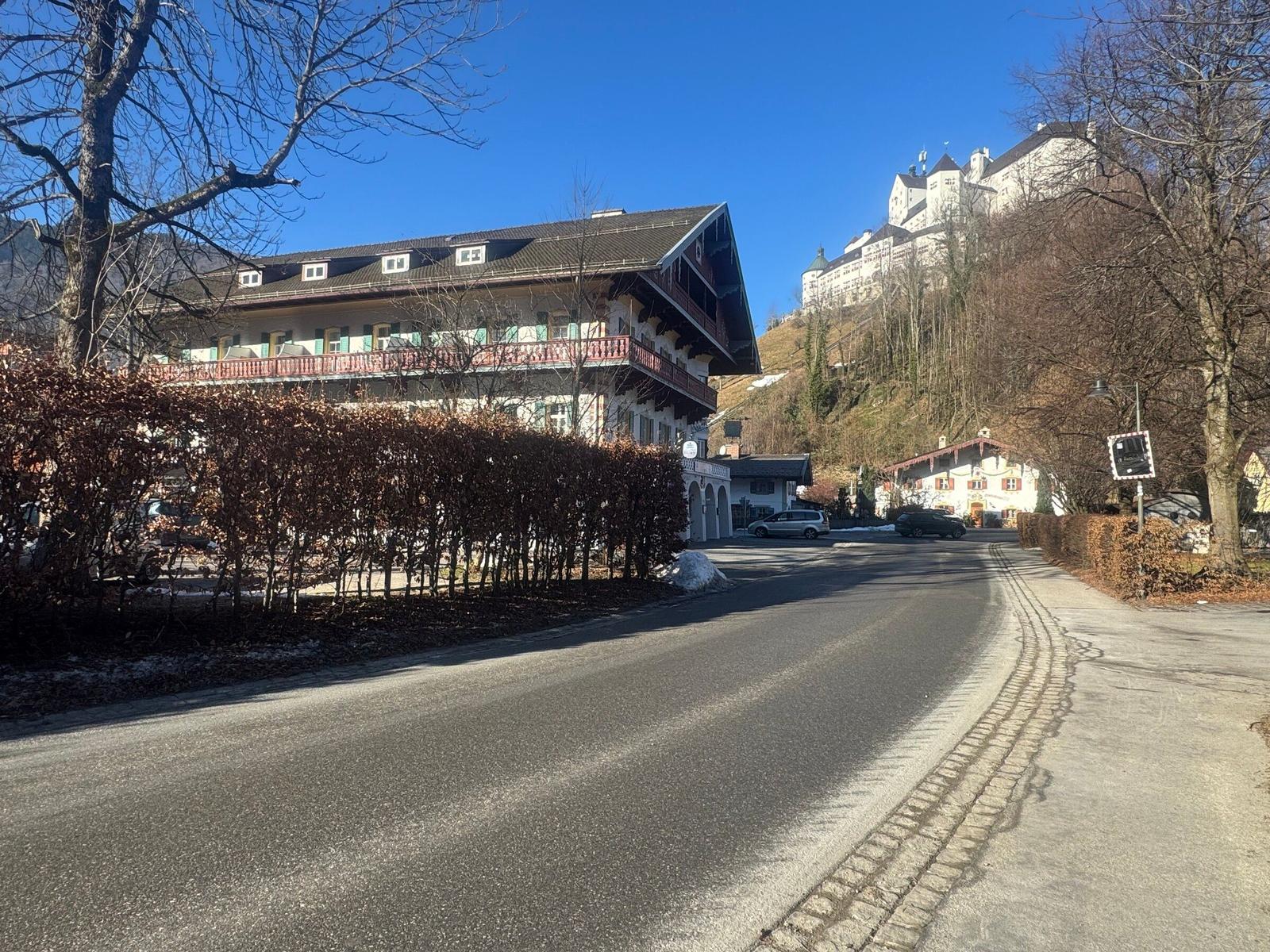 Haus mit Balkon und Straße, im Hintergrund Burg auf Hügel.