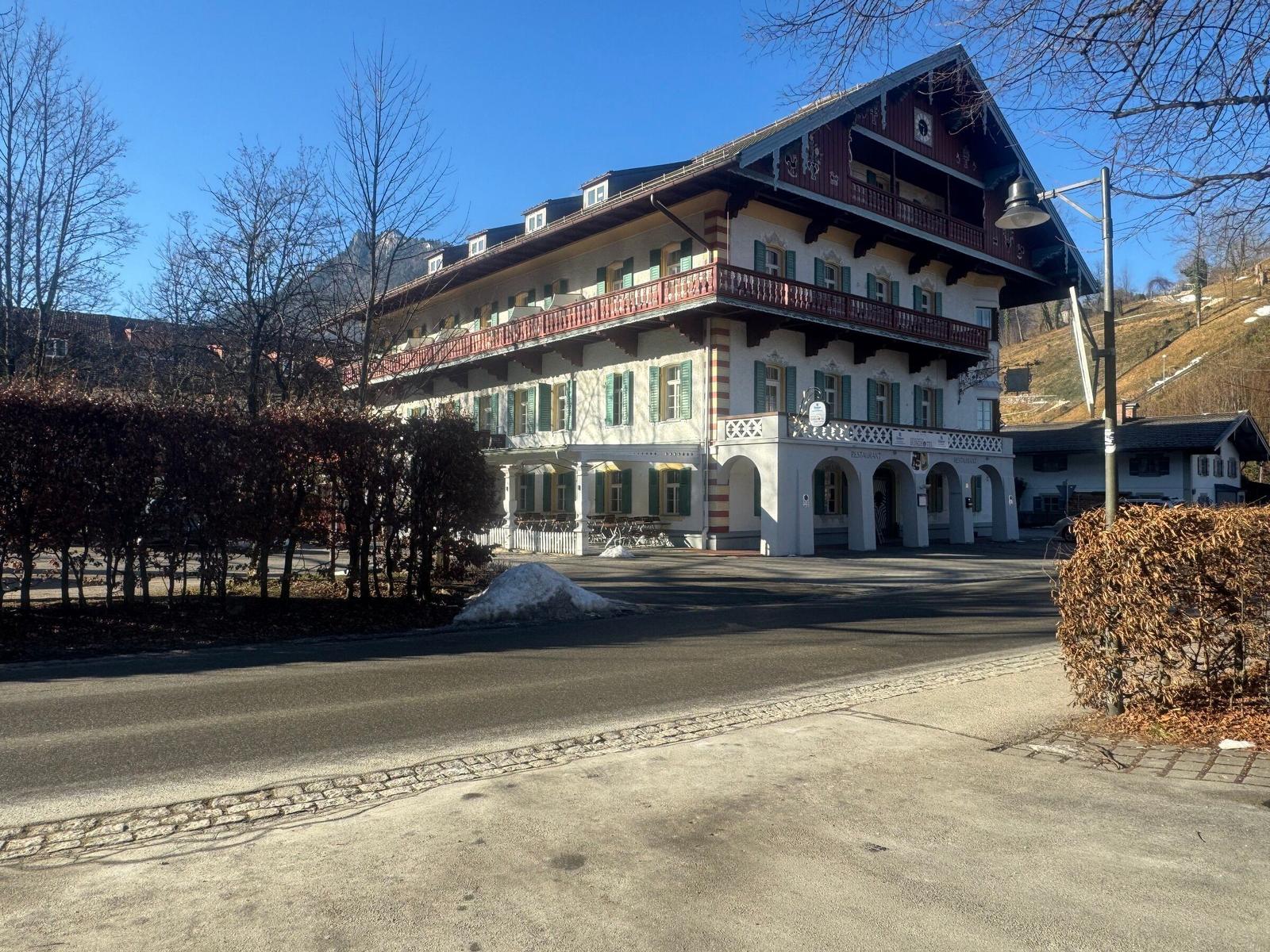 Traditionelles Gebäude mit Balkonen und grünen Fensterläden. Schnee liegt vor dem Eingang.