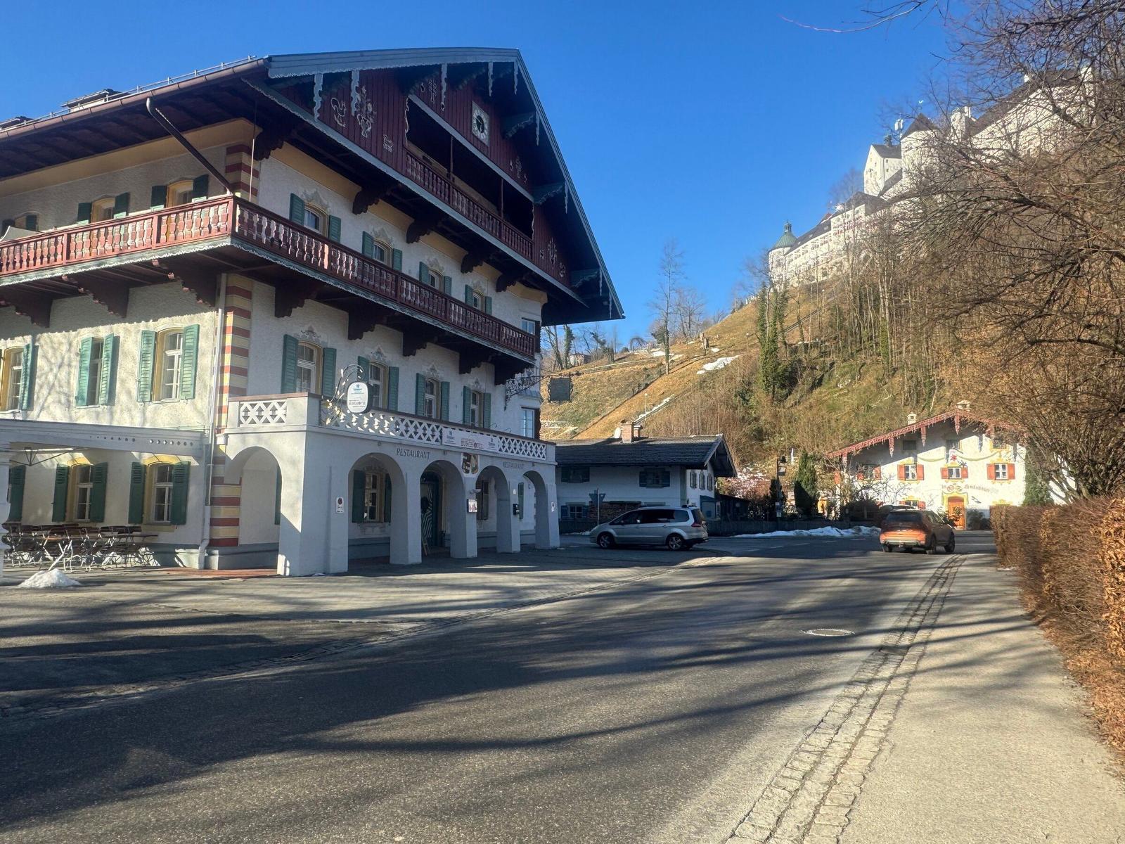 Haus mit Balkon und Restaurant im Dorf, Schloss auf Hügel im Hintergrund.