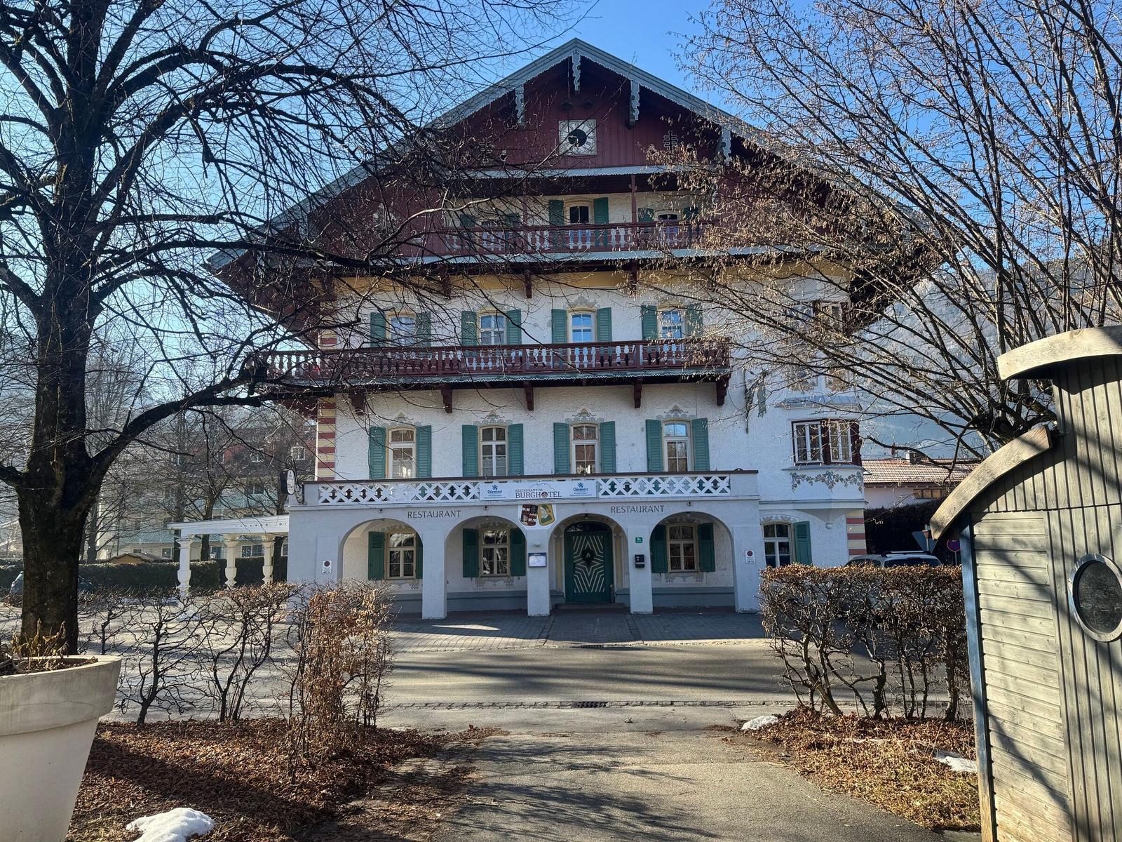 Traditionelles Hotel mit Balkonen und grünen Fensterläden. Eingangsbereich mit Arkaden.