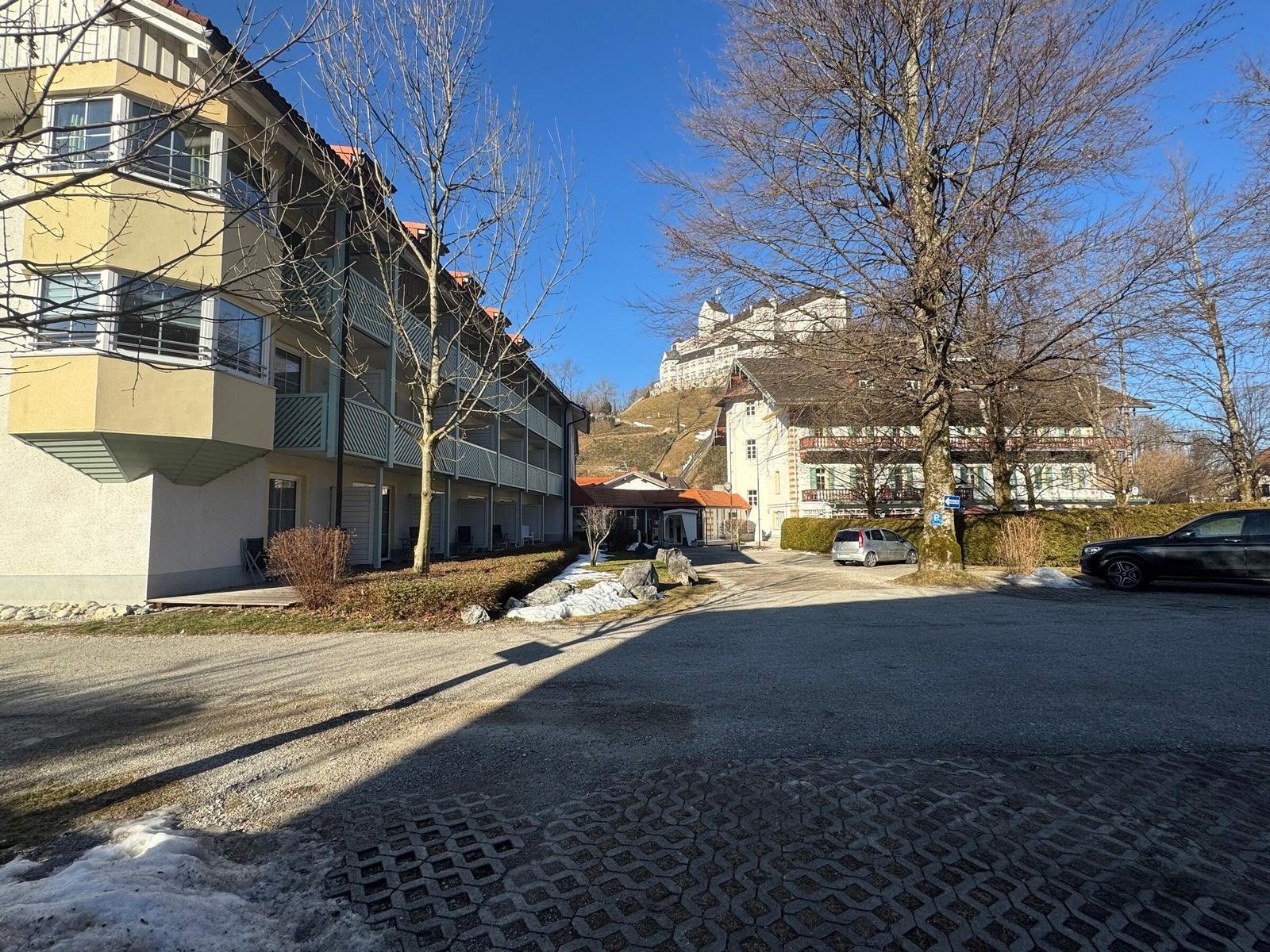 Vor dem Haus liegt ein Parkplatz mit Bäumen und Schnee. Im Hintergrund ist ein Schloss auf einem Hügel.