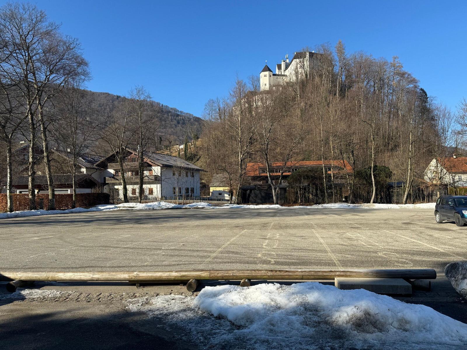 Parkplatz mit Schneehaufen, Hintergrund: Dorf und Burg auf Hügel