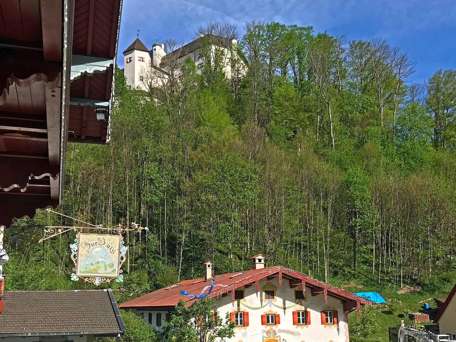 Schloss auf Hügel mit Wald, traditionelle Häuser im Vordergrund