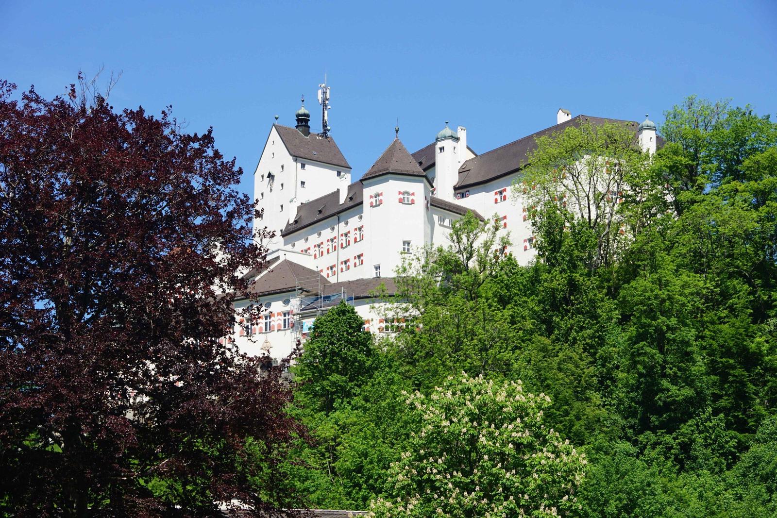 Weißes Schloss mit roten Fensterläden und grüner Umgebung.