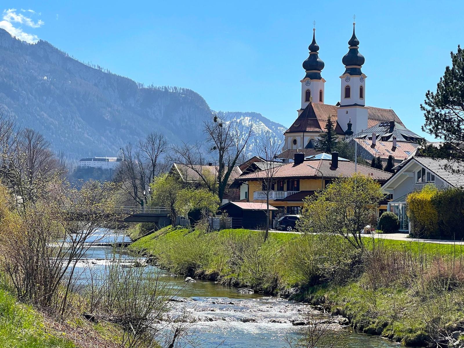 Flussufer mit Kirche und Bergen im Hintergrund