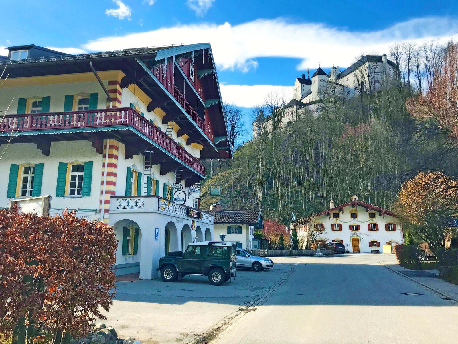 Altes Haus mit Balkon und Schloss auf Hügel im Hintergrund.