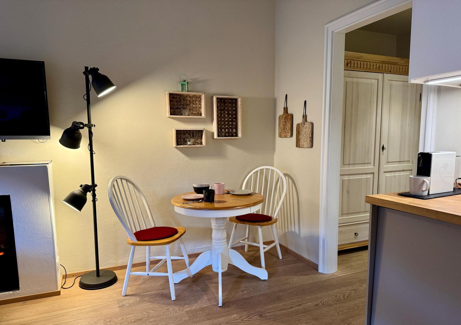 Kleine Essnische mit runden Tisch und zwei Stühlen. Im Hintergrund Küche und Schrank.