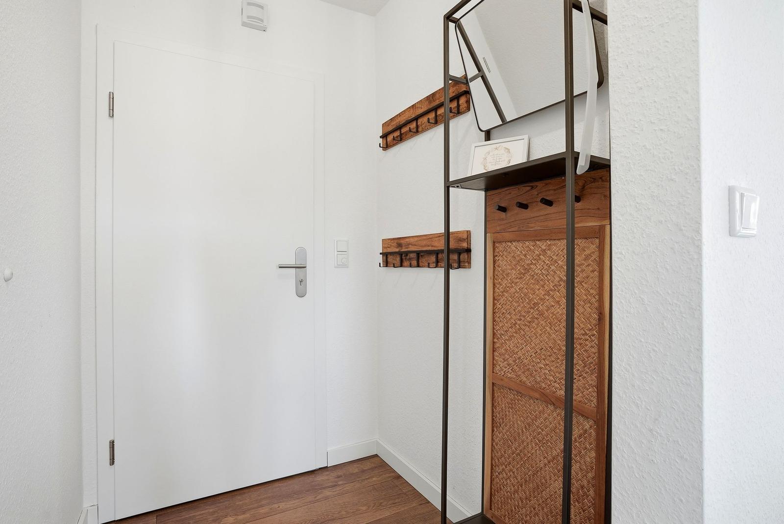Eingangsbereich mit weiße Tür, Holzfußboden und Spiegelschrank mit Körbchen.