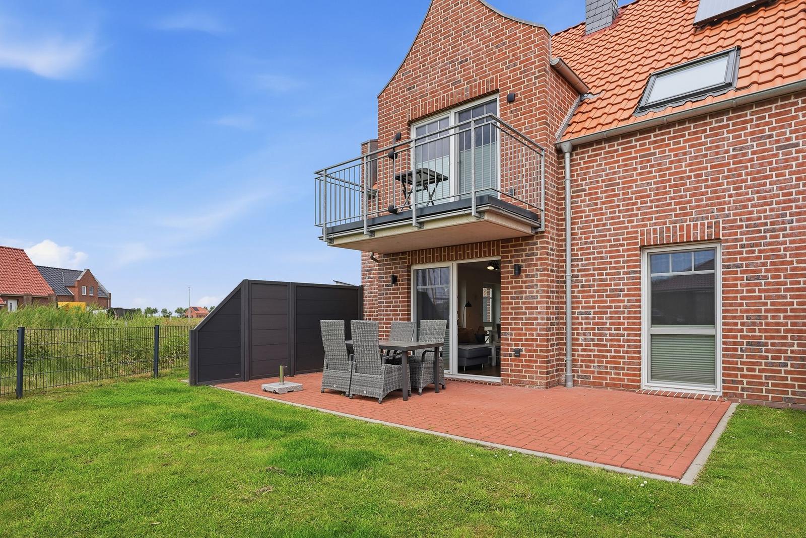 Roter Ziegelbau mit Balkon und Terrasse mit Gartenmöbeln und grünem Rasen.