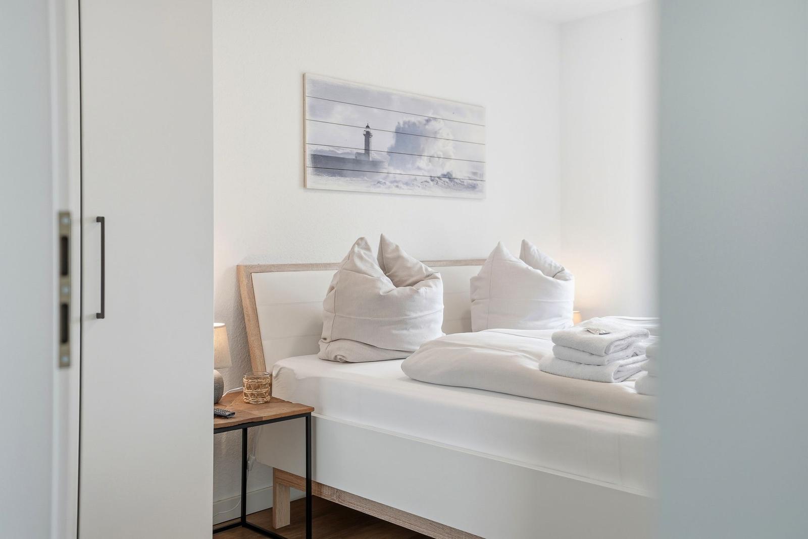Schlafzimmer mit weißem Bett, dekorativer Wandkunst und Nachttisch mit Lampe.