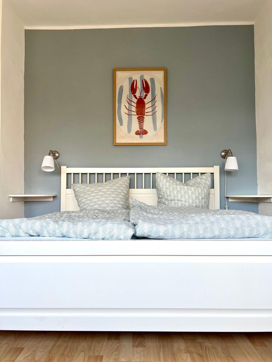 Schlafzimmer mit weißem Bett, grauer Wand und einem Bild eines Hummers.