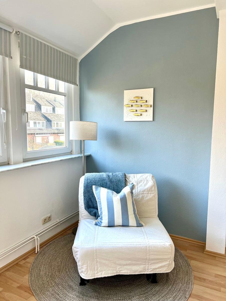 Ein Sessel mit Kissen und Decke steht auf einem runden Teppich vor einem Fenster.