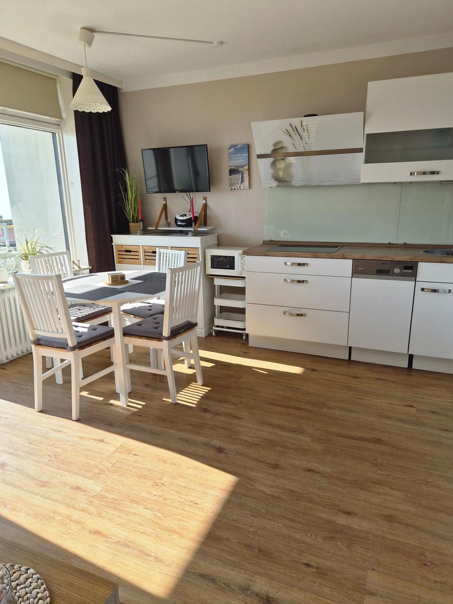 Küche und Essbereich mit Tisch, Stühlen und Fernseher. Holzboden und große Fenster.