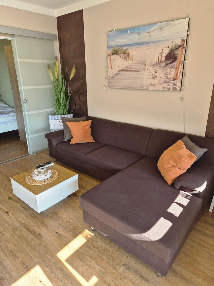 Wohnzimmer mit braunem Sofa, Holzboden und Wandbild mit Strandmotiv.