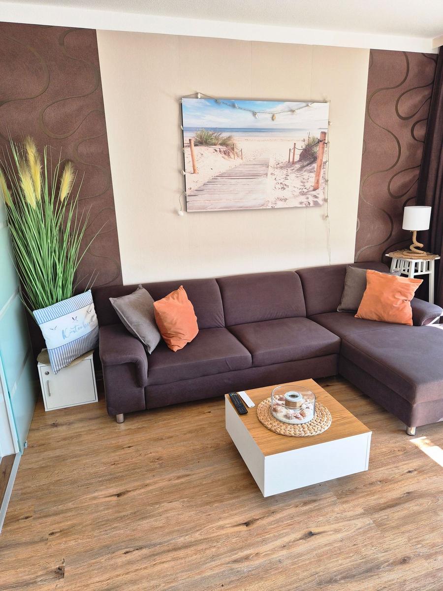Ein Wohnzimmer mit braunem Sofa, Holzboden und Wandbild eines Strandes.