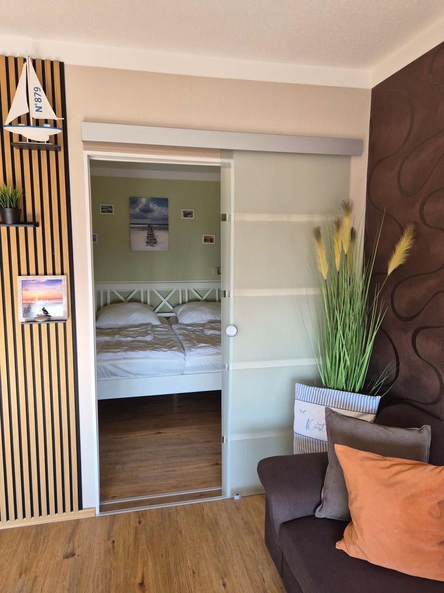 Schlafzimmer mit Doppelschlafcouch und Holzboden. Wohnbereich mit Sofa und Pflanze.