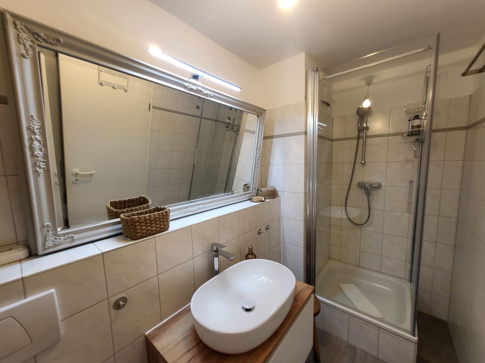 Badezimmer mit Dusche, Waschbecken und Spiegel