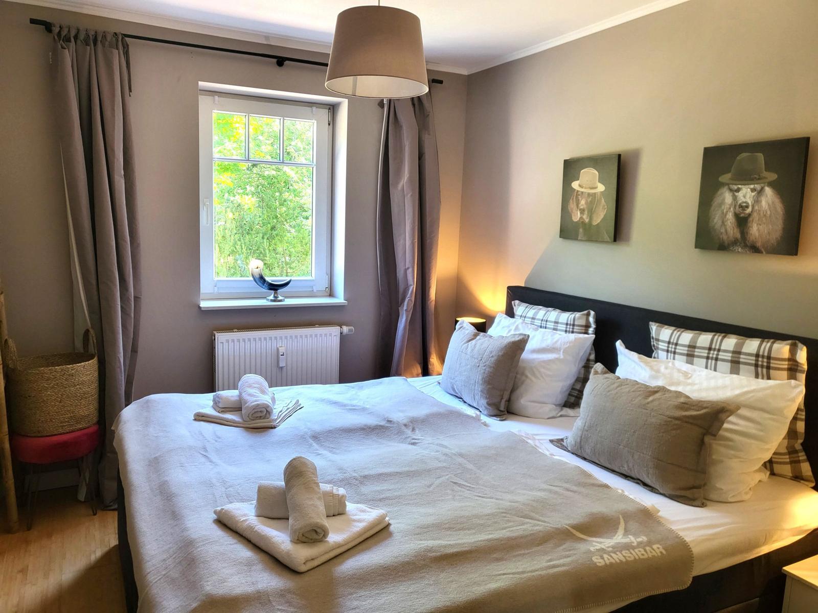 Schlafzimmer mit Bett, Fenster, Wandbildern und Handtüchern.
