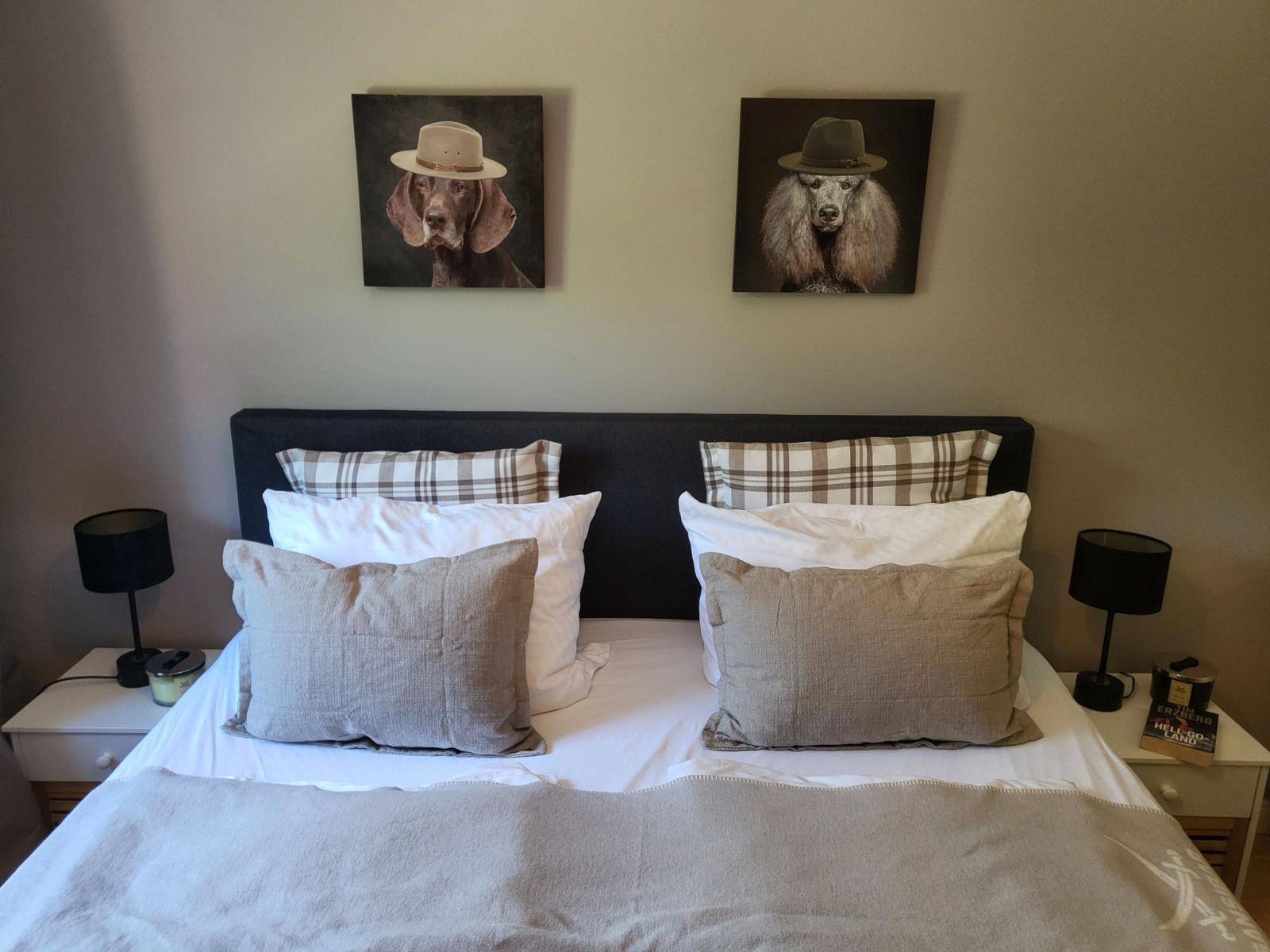 Schlafzimmer mit Bett, zwei Nachttischen und Wandbildern von Hunden.