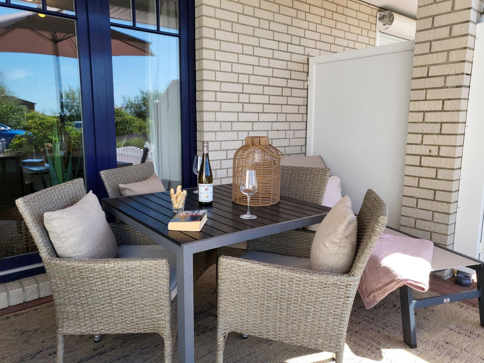 Terrasse mit Tisch und Stühlen, Weinflasche und Buch.