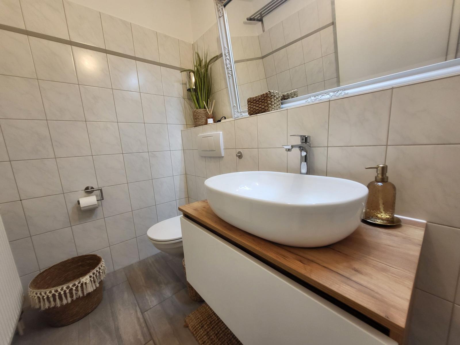 Bad mit Waschbecken auf Holzoberfläche, Spiegel und Toilette.