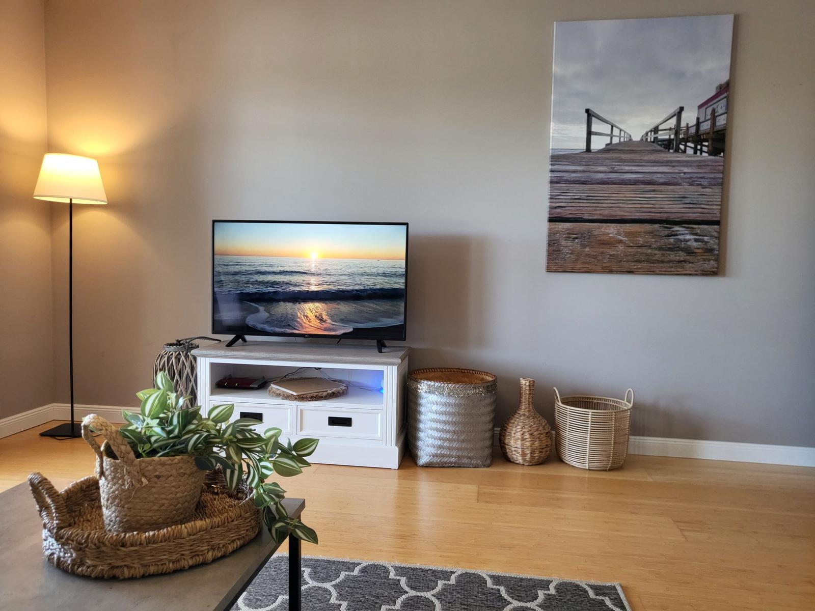 TV auf weißen Schrank, Wandbild mit Pier, Körbe und Pflanze auf Tisch