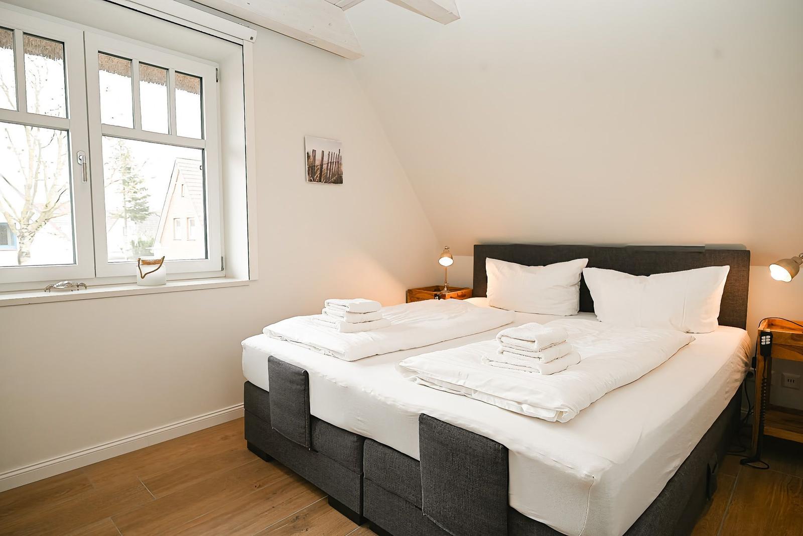 Schlafzimmer mit Doppelbett, Fenster und Holzboden.