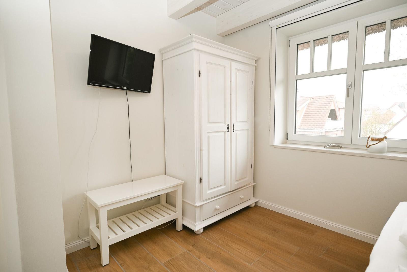Zimmer mit weißem Schrank, Wand-TV und Fenster mit Blick auf Dächer.