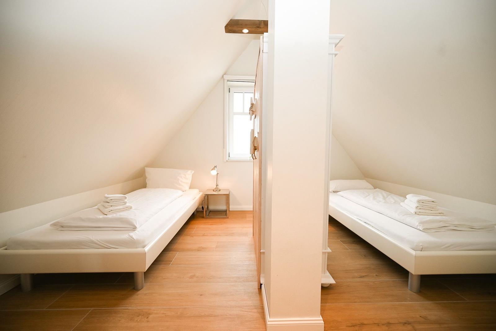 Zwei Schlafplätze mit weißen Matratzen und Bettwäsche in einem Dachzimmer mit Holzboden und Fenster.