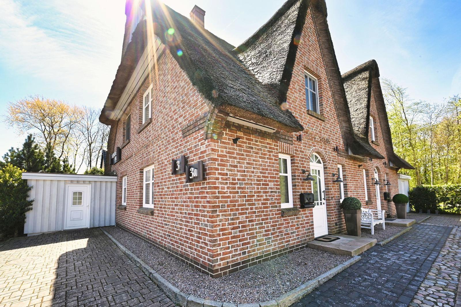 Rotes Backsteinhaus mit Strohdach, weiße Türen und Fenster, gepflastertes Vorfeld und Garten.