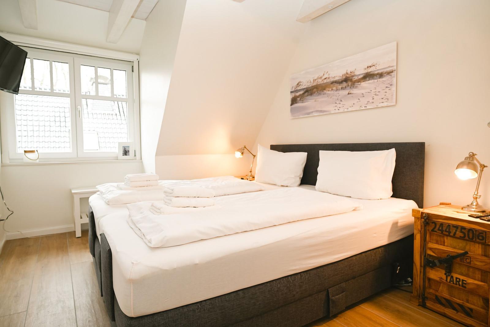 Schlafzimmer mit Bett, Nachttisch und Fenster. Decke ist schräg.