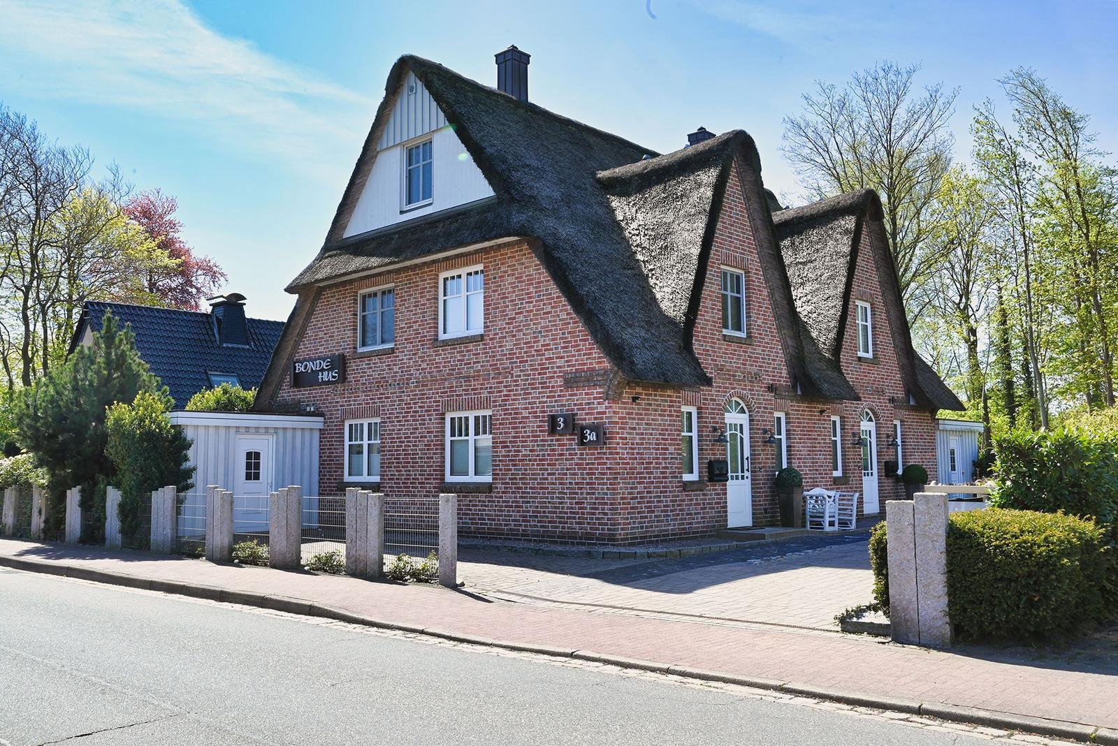 Rotes Backsteingebäude mit Strohdach und weißen Fenstern an Straße