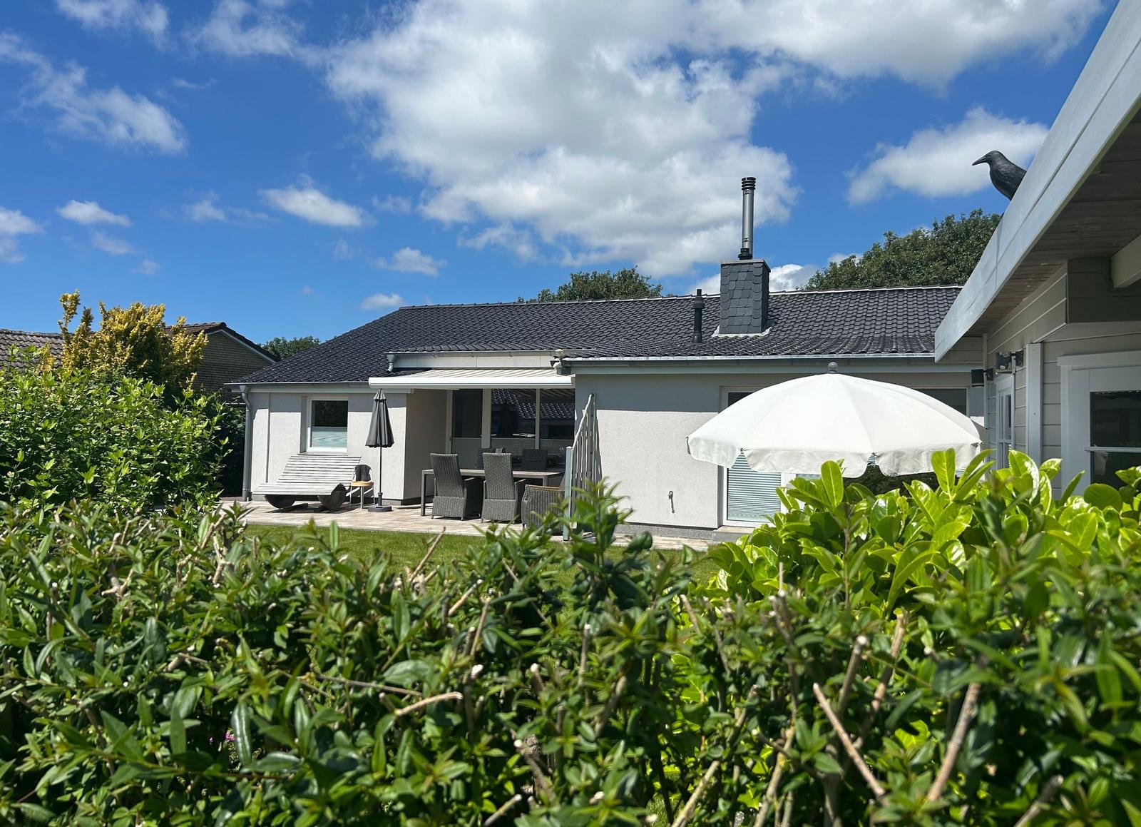 Wohnhaus mit Terrasse, Garten und Sonnenschirm unter blauem Himmel.
