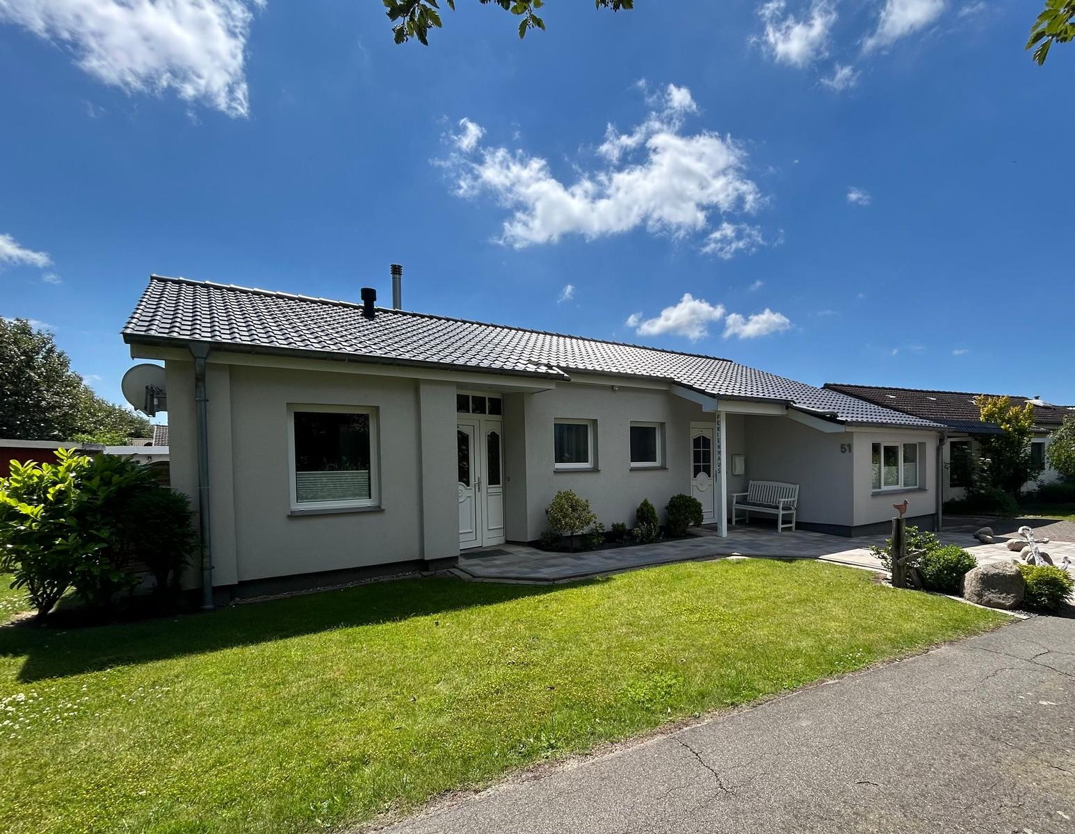 Ein Einfamilienhaus mit Garten, Terrasse und weißen Fenstern unter blauem Himmel.