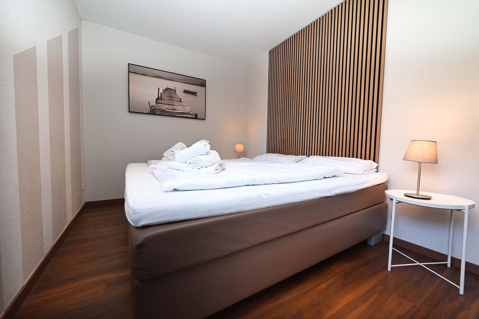 Schlafzimmer mit Bett, Nachttisch und Wandbild.