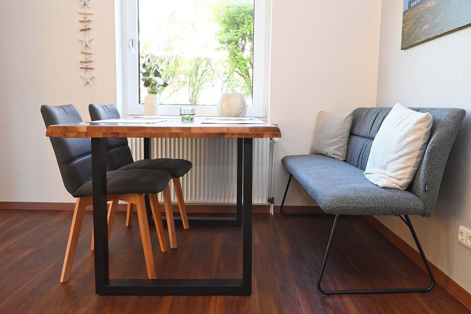 Essbereich mit Tisch, zwei Stühlen und Sofa. Fenster mit Blick auf Garten.