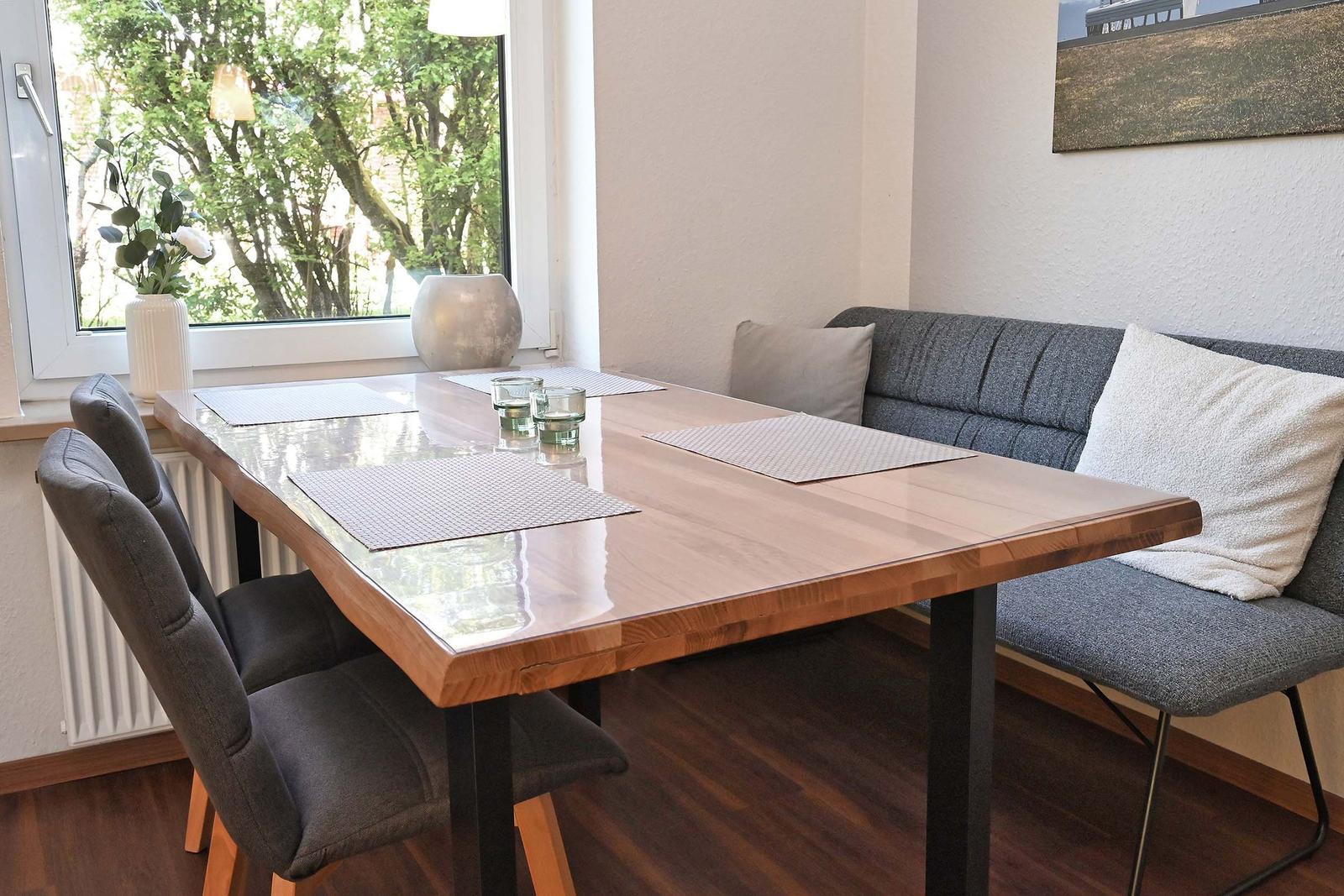 Esstisch mit Bank und Stühlen vor Fenster mit Blick auf Bäume.