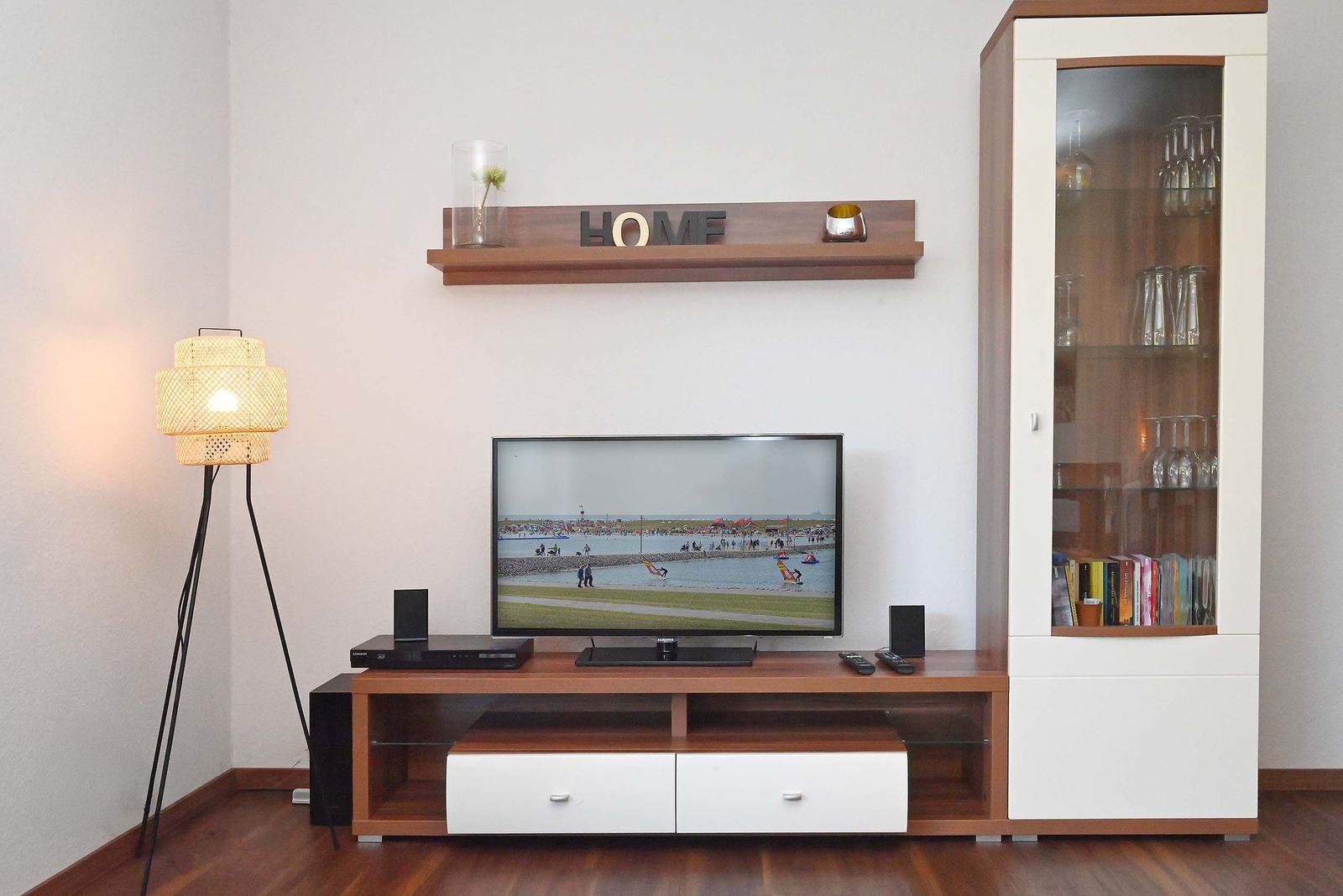 TV auf Holzregal mit Glasfrontschrank und Stehlampe. Wandregal mit Dekoration.
