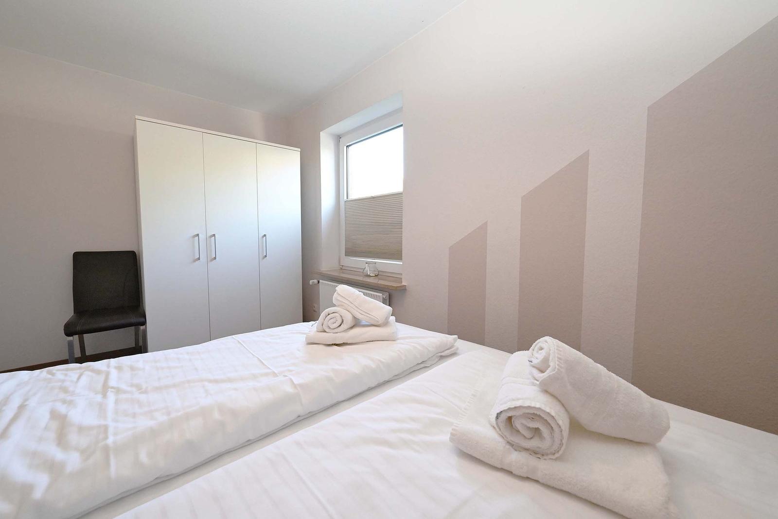 Zimmer mit zwei Betten, Kleiderschrank und Fenster. Handtücher auf den Betten.