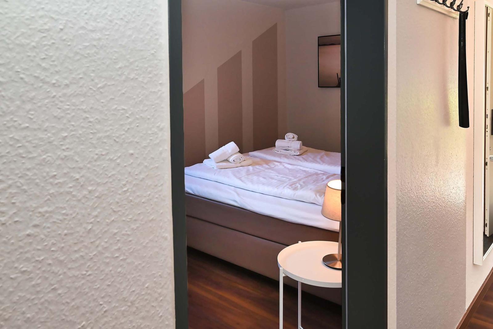 Schlafzimmer mit Doppelbett, weißen Bettwäsche und Handtüchern, kleiner Tisch und Lampe.