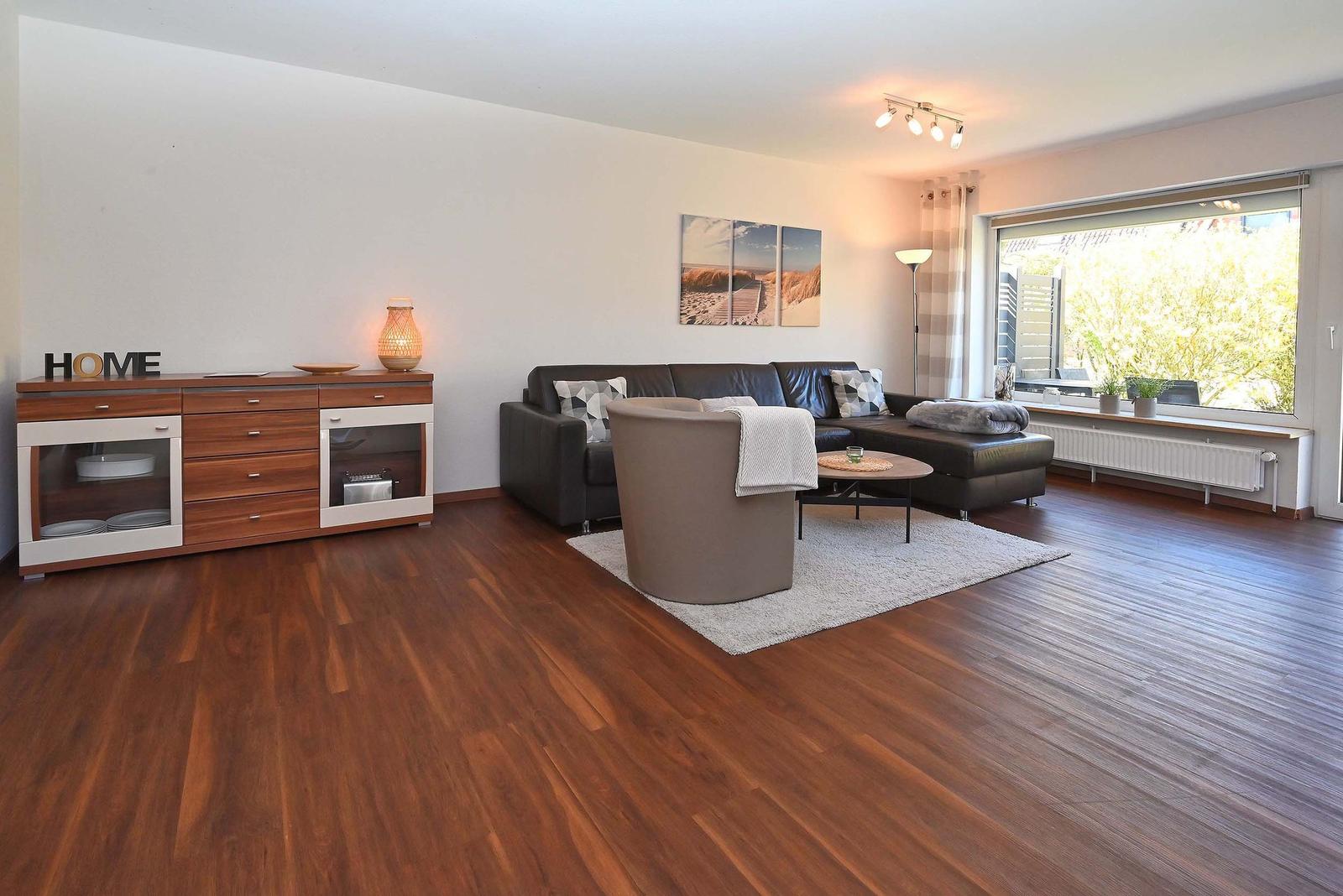 Wohnzimmer mit Sofa, Sessel, Couchtisch und Holzboden. Große Fensterfront mit Blick.