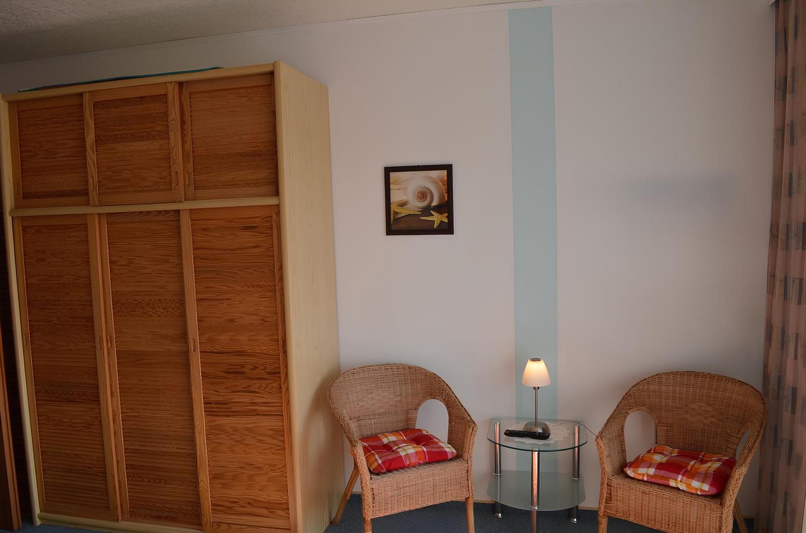 Zimmer mit Holzschrank, zwei Stühlen und Tisch mit Lampe.