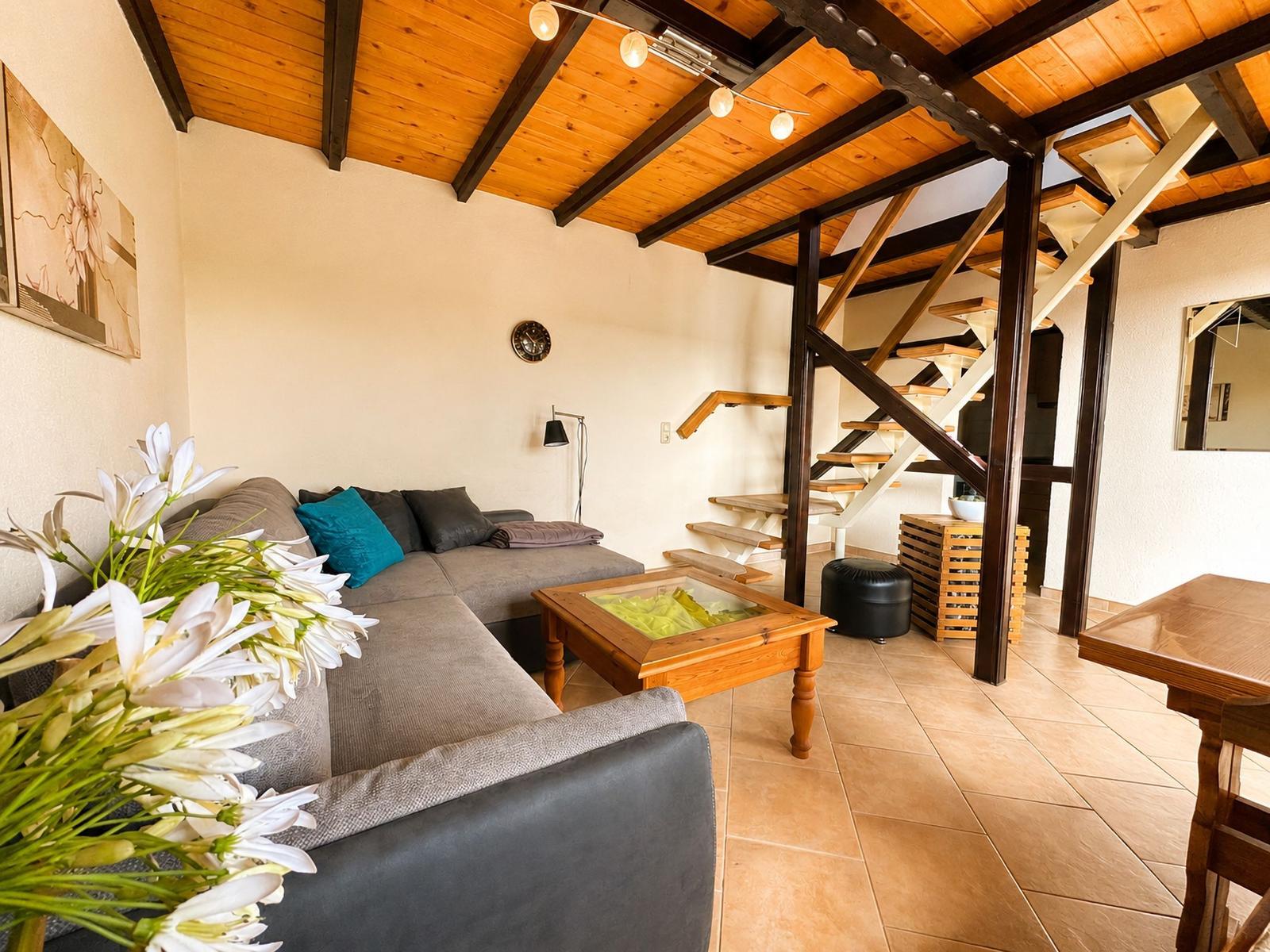 Wohnzimmer mit Sofa, Couchtisch und Treppe zur oberen Etage.