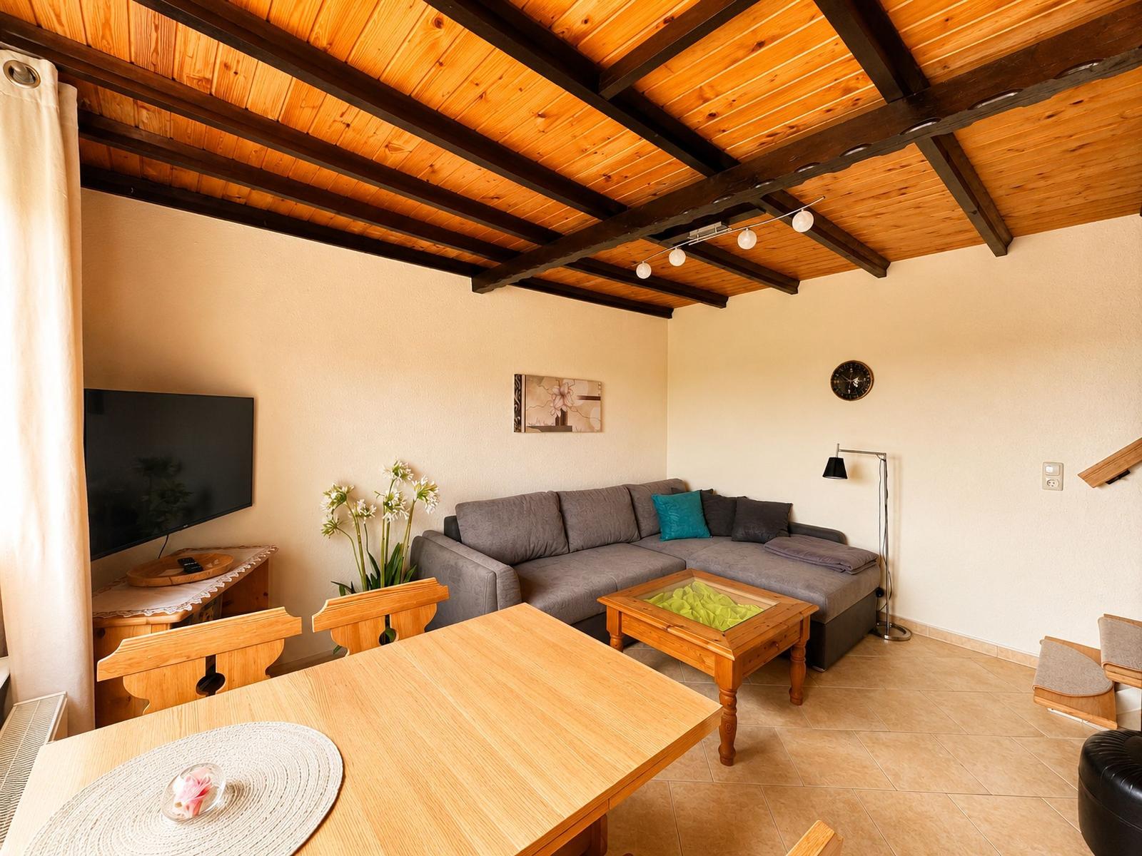 Wohn- und Essbereich mit Sofa, Esstisch und Holzdecke.