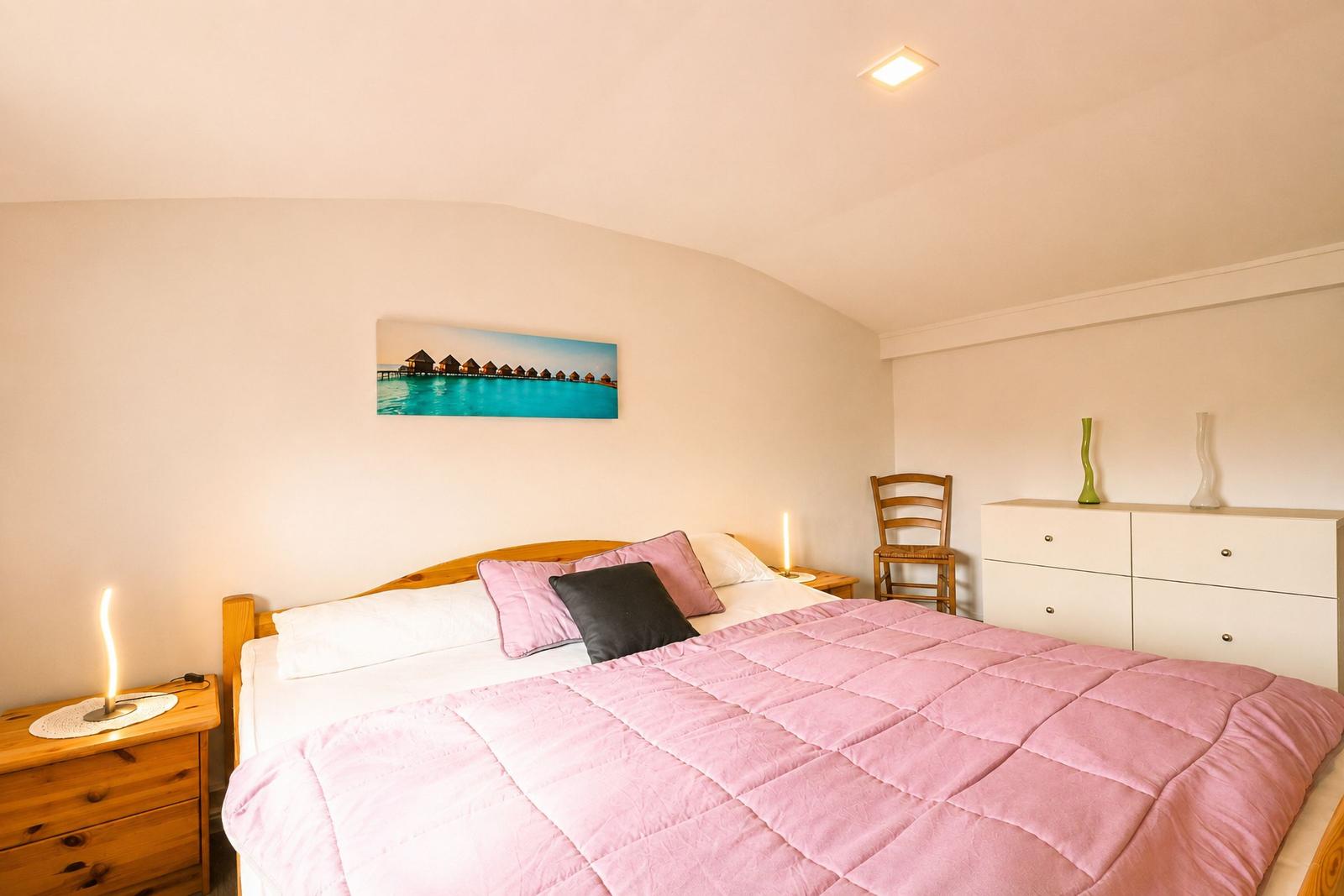 Schlafzimmer mit Bett, Nachttisch und Schrank. Wandbild zeigt Wasserhütten.
